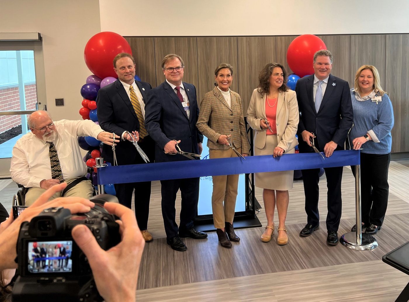 A line of people hold scissors to cut a blue ribbon to designate the opening of Patricia Neal Rehabilitation Hospital West.